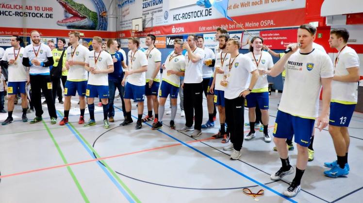 Die Empor-Handballer im Schmuck ihrer Meistermedaillen. Den Dank  an die Fans und an Trainer Till Wiechers (rechts) bringt mit dem Mikrofon in der Hand Tim Völzke als Beauftragter des Mannschaftsrates zum Ausdruck.