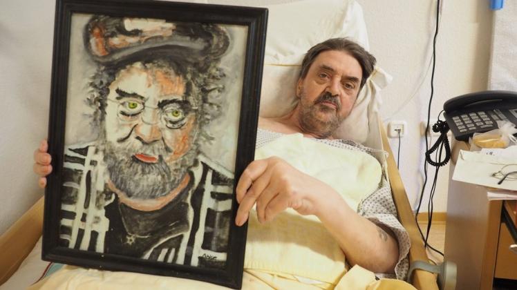 Jörg Abke in seinem Pflegebett. Er hält ein Selbstportrait, das 2015 entstand.