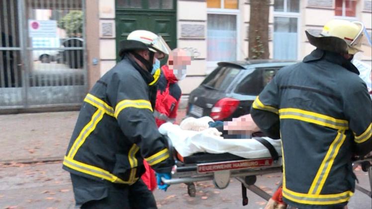 Feuerwehrleute und ein Sanitäter bringen einen am Bein verletzten Mann zum Rettungswagen.