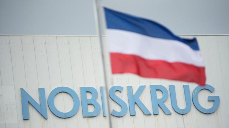 Nobiskrug: Der Firmenname der Werft ist auf einer Werkshalle vor einer Fahne in den Landesfarben von Schleswig-Holstein zu sehen.