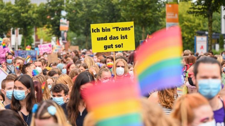 Demonstranten und Demonstrantinnen ziehen während des Christopher Street Day 2021 durch Oldenburg. Eine von ihnen hält währenddessen ein Schild mit der Aufschrift «Ich bin »Trans« und das ist gut so!» hoch. Foto: Mohssen Assanimoghaddam/dpa