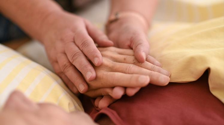 Eine Hospizmitarbeiterin hält die Hand eines todkranken Menschen.