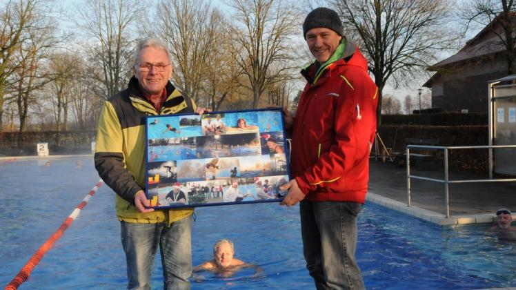 Am Beckenrand übergibt Karl-Heinz Rohrmann die Collage mit Bildern aus der Freibadsaison von Gertrud Premke, an Schwimmmeister Dirk Wichmann.