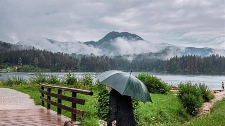 Eine Frau geht bei Regen mit ihrem Hund am Hintersee in Ramsau Bei Berchtesgaden spazieren. 
