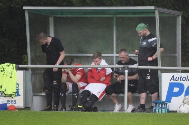 Die Auswechselspieler des Heidmühler FC suchten Schutz während einer der starken Wolkenbürche. Foto: Rolf Tobis