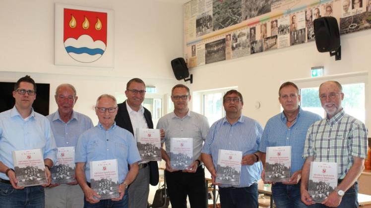 Vor dem Wappen und der Zeitleiste, die gleichzeitig als Schallschutz dient und mit Unterstützung der Bürgerstiftung Salzbergen realisiert werden konnte, präsentierten die „ Macher“ die  Vereinschronik. Sie ist ab sofort zum Preis von 20 Euro zu erwerben. Foto: Anne Bremenkamp