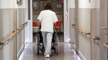 Eine Pflegerin schiebt eine Frau in ihrem Rollstuhl durch den Gang eines Altenheims in Düsseldorf. Eine neue Studie hat untersucht, wie unterschiedlich die Länder mit Informationen über Pflegeheime umgehen. Für Betroffene und Angehörige ist das ein Problem.