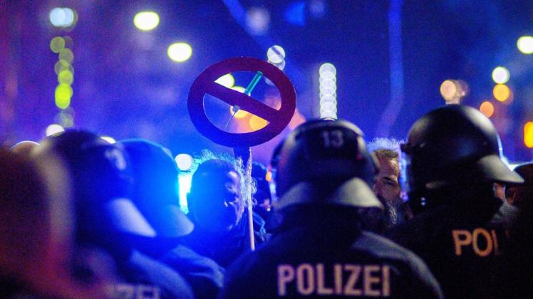 Polizisten und und Demonstranten stehen sich in der Innenstadt von Magdeburg gegenüber. Dabei trägt ein Demonstrant eine Schild, das eine durchgestrichene Spritze zeigt. Bundesweit gingen zu Wochenbeginn Zehntausende auf die Straßen, um gegen Corona-Maßnahmen zu protestieren. Nicht immer blieben die Aufzüge friedlich.