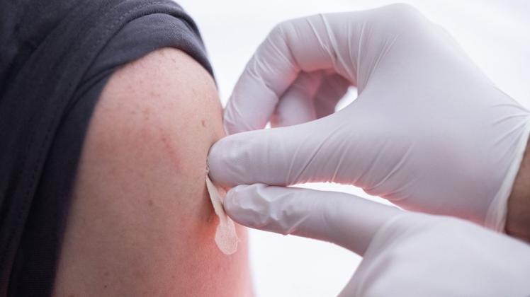 Eine geimpfte Person bekommt vom Arzt einen Pflaster auf die Nadeleinstichstelle am Oberarm.