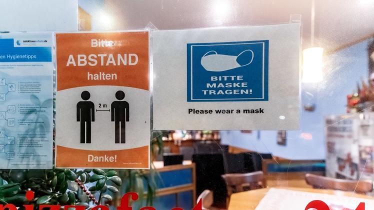 Zettel mit de Aufschriften „Bitte Abstand halten“ und „Bitte Maske tragen“ hängen an der Tür eines Lokals.