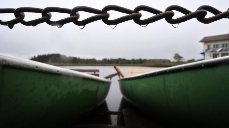 Ruderboote eines Bootsverleihes liegen am Ufer des Elbsees in Bayern im Regen. Ruderboote eines Bootsverleihes liegen am Ufer des Elbsees in Bayern im Regen.