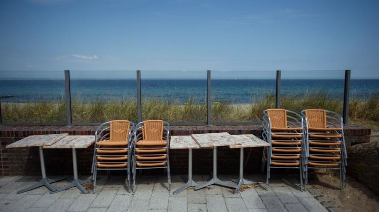 Timmendorfer Strand: Tische und Stühle stehen zusammengebunden auf der Terrasse mit Meerblick eines Restaurants an der Strandpromenade in Niendorf.