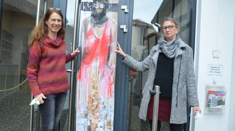Kerstin Schumann (links) und Andrea Wilmers präsentieren das erste Motiv der neuen Ausstellungsreihe im Fenster.