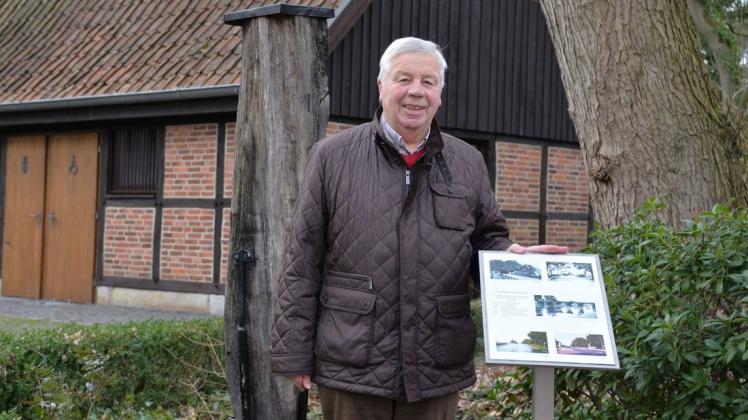 Willi Terhorst, Vorsitzender des Heimatvereins Schepsdorf, steht zwischen einem Gründungspfahl der 1824 errichteten Holzbrücke und einer dazugehörigen Infotafel vor dem Heimathaus des Lingener Ortsteils.
