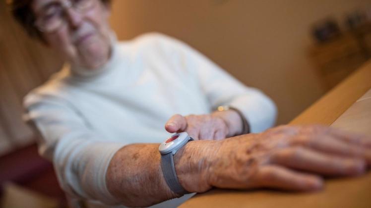 Eine Seniorin drückt den Notrufknopf am Notfallarmband für den Hausnotruf.