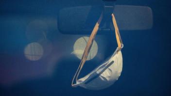 Eine Maske hängt am Rückspiegel eines Autos. (Symbolfoto)