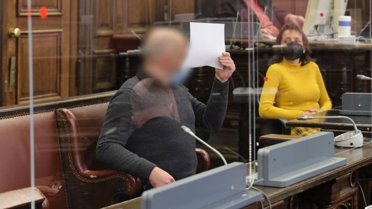 Der Angeklagte hält sich in einem Gerichtssaal des Strafjustizgebäudes in Hamburg ein Blatt Papier vor das Gesicht.