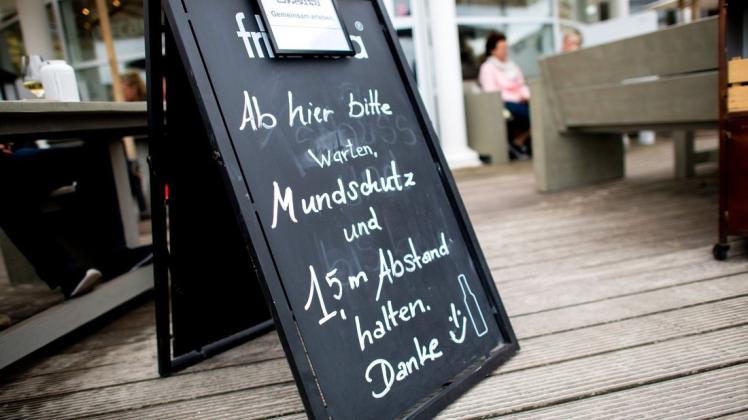 Niedersachsen, Norderney: Ein Schild mit der Aufschrift ·Ab hier bitte warten, Mundschutz und 1,5m Abstand halten. Danke· steht am Zugang zum Surfcafe an der Strandpromenade. Hotels, Ferienwohnungen und andere Quartiere in niedersächsischen Regionen mit einer Sieben-Tage-Inzidenz unter 100 dürfen wieder Gäste empfangen. Buchen können zunächst nur Menschen aus Niedersachsen. Foto: Hauke-Christian Dittrich/dpa +++ dpa-Bildfunk +++