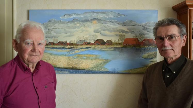 Die beiden ehemaligen Schulkameraden Willfried Jahnke und Horst Kühne (r.) beschäftigen sich mit der Geschichte ihres Heimatdorfes Rosien, das im Hintergrund in einer Malerei erkennbar ist.