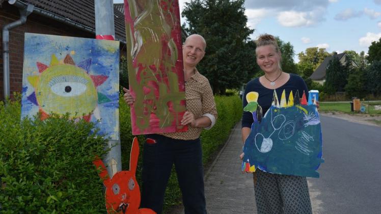 Barbara Wetzel (l.) und Julia Marx vom Allerhand-Verein zeigen einige der Bilder, die für die Straßenkunstausstellung in Qualitz vorbereitet wurden.