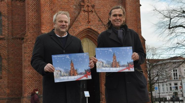 Helmut Greve (l.) und Detlev Hammerschmidt vom Lions Club Warnemünde präsentieren an Ort und Stelle den diesjährigen Adventskalender, den in diesem Jahr die Kirche des Ostseebades ziert.