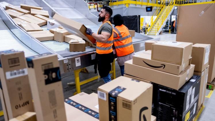 Mitarbeiter des Paketversenders Amazon sortieren Pakete.