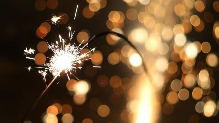 Symbolbild: Eine große Wunderkerze brennt in der Silvesternacht vor einer gezündeten Silvesterrakete.  Das Feuerwerk gehört eigentlich wie die Party zum Jahreswechsel. Doch dieses Jahr wird vieles eingeschränkt.