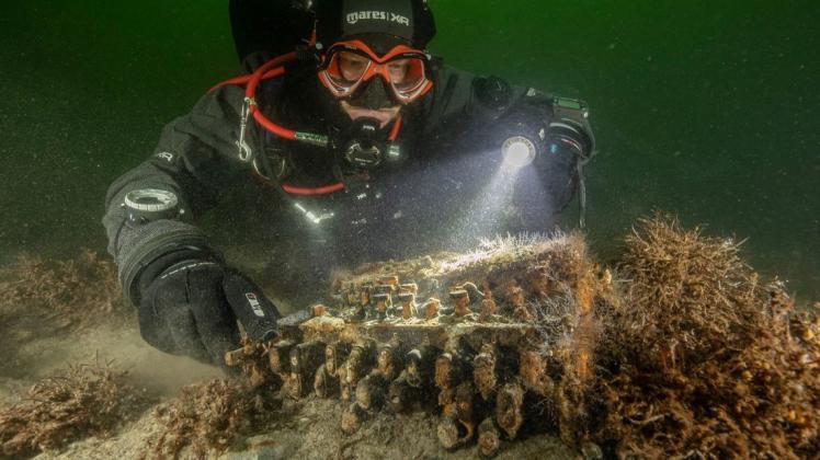 Der Unterwasserarchäologe und Taucher Florian Huber auf dem Grund der Ostsee mit der Enigma-Chiffriermaschine aus dem Zweiten Weltkrieg.