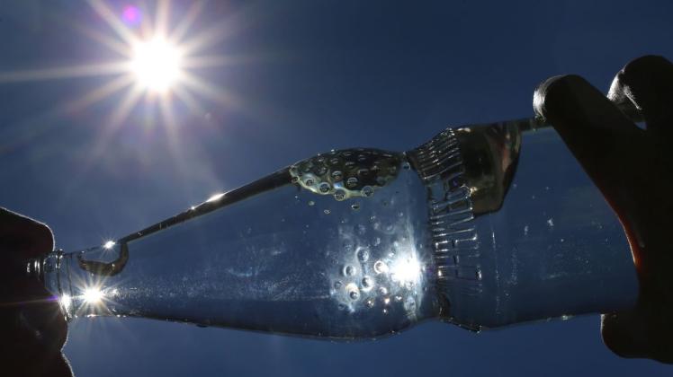 Eine Frau trinkt im Sonnenschein aus einer Flasche sprudelndes Mineralwasser.