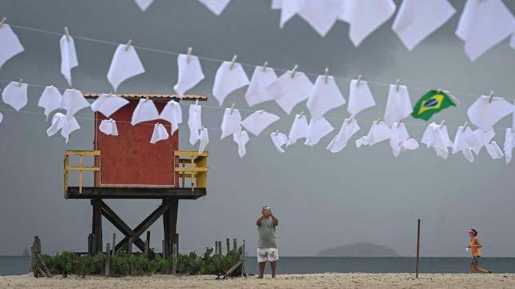 Ein Mann fotografiert bei einer Protestaktion zum Gedenken an die Menschen, die in Brasilien an Covid-19 gestorben sind, weiße Taschentücher, die am Copacabana-Strand aufgehängt wurden. In Brasilien wurden bereits mehr als 600.000 Todesfälle verzeichnet.