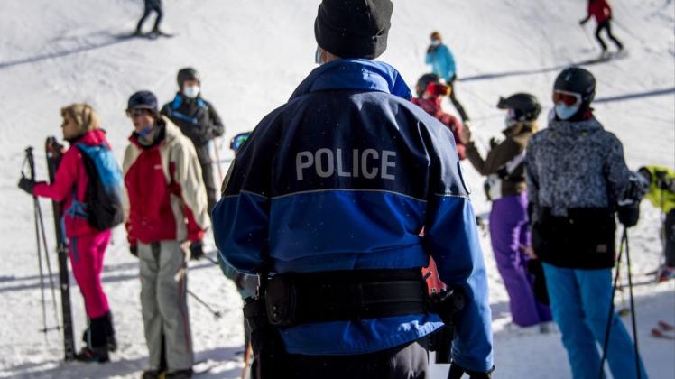 Ein Polizist kontrolliert Ski-Fahrer auf einer Piste im Walliser Skigebiet auf das Tragen von Mund-Nasen-Bedeckungen (Archivbild).