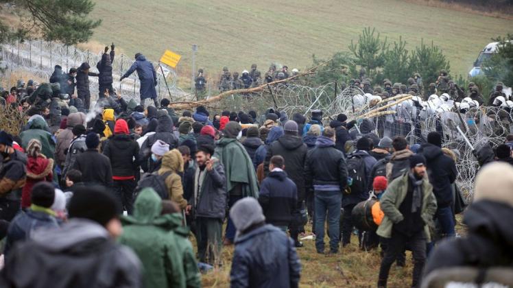 Polnische Polizisten stehen hinter einem Stacheldrahtzaun, während sich an der weißrussisch-polnischen Grenze Migranten versammelt haben. Mehrere Hundert Migranten haben sich nach Angaben der Behörden in Belarus zu Fuß auf den Weg zur Grenze zum EU-Nachbarland Polen gemacht.