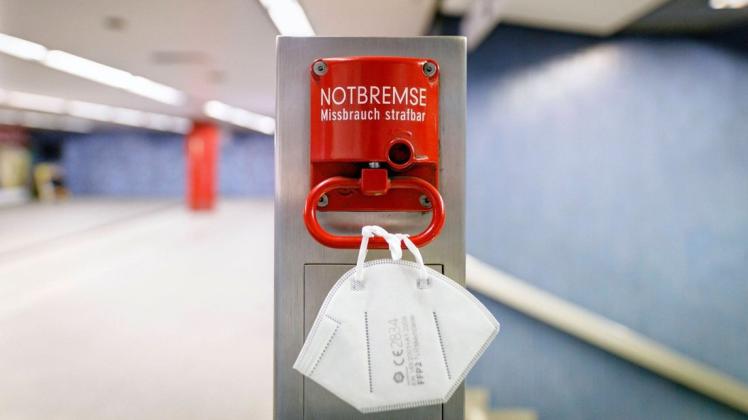 An einer Notbremse in einer Bahnhaltestelle hängt eine FFP2-Maske. Der Bundestag soll am kommenden Mittwoch über die sogenannte Bundes-Notbremse entscheiden.