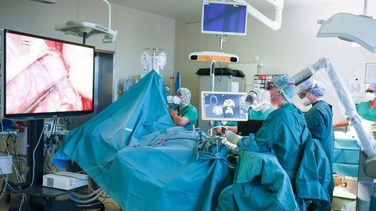 Die Spezialisten des OP-Teams der Neurochirurgie nutzen bei einer Gehirn-Operation das hochmoderne Videosystem. Auf dem großen Bildschirm (links) wird das OP-Feld vergrößert dargestellt. Das Kamerasystem „Orbeye“ steht rechts vom Operateur, der mit einer 3-D-Brille arbeitet.