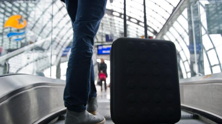 Eine Person steht mit einem Koffer auf einer Rolltreppe