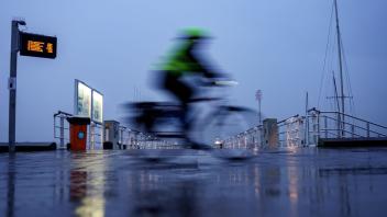 Kiel: Ein Radfahrer passiert im strömenden Regen einen Bootsanleger am Ufer der Förde.