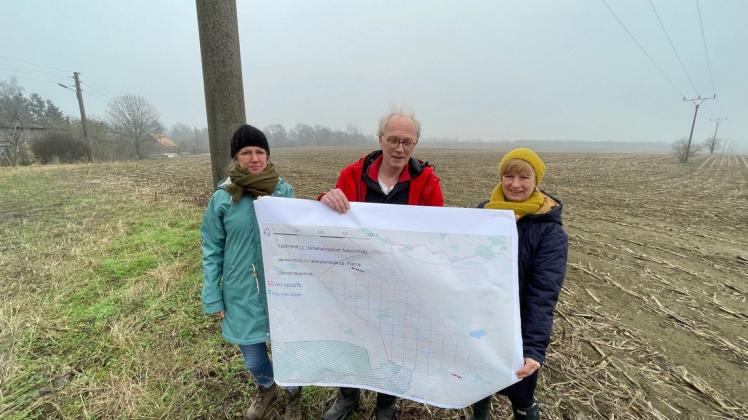 Jana Müller sowie Theo und Birgit van Meegen (v.l) mit einer selbstgefertigten Karte, auf der das Areal gekennzeichnet ist, das betroffen ist. Im Hintergrund die Fläche auf der die Photovoltaik-Anlage entstehen soll.