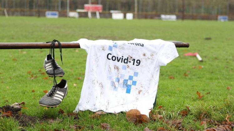 Ein weißes Fußballtrikot mit der Aufschrift Covid-19 liegt auf der Auswechselbank eines Sportplatzes. In Brandenburg dürfen Kicker jetzt wieder nach der 3G-Regel spielen. Doch bei Sonntagspartien fällt es mangels geöffneter Testzentren schwer, die Testkriterien einzuhalten.