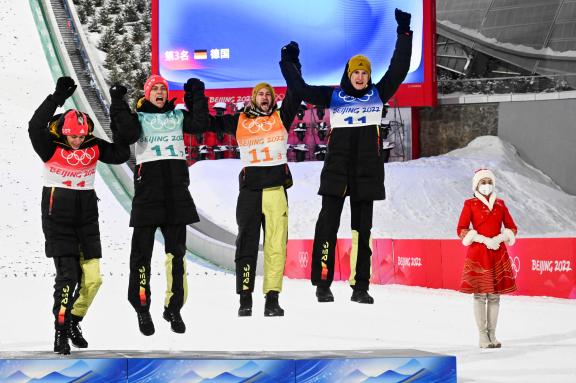 Third placed Germany from left, Germany&apos;s Constantin Schmid, Germany&apos;s Stephan Leyhe, Germany&apos;s Markus Eisenbichler and Germany&apos;s Karl Geiger leaps omto the podium to celebrate celebrate during the victory ceremony following the Ski Jumping Men&apos;s Team Final, on February 14, 2022 at the Zhangjiakou National Ski Jumping Centre, during the Beijing 2022 Winter Olympic Games. (Photo by Christof STACHE / AFP)