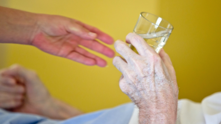 Hilfe im Alltag: Eine Pflegerin reicht einem Patienten ein Glas Wasser.  
