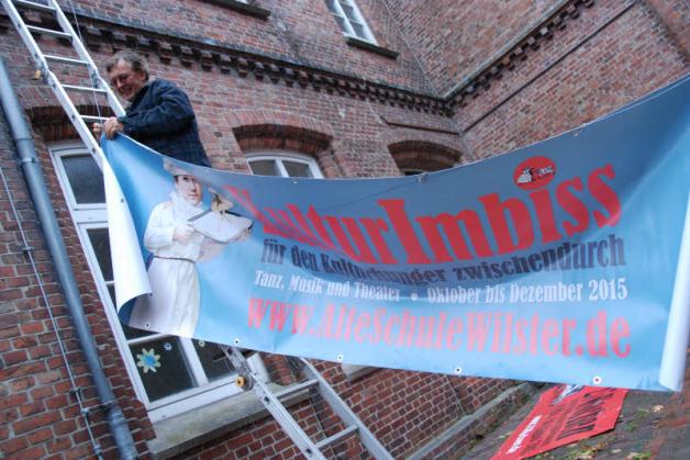 Auf 25 Wochen Tanz und Theater in der Wilstermarsch folgt ein KulturImbiss bis Dezember. Carsten Döhler befestigt das neue Transparent an der Alten Schule.