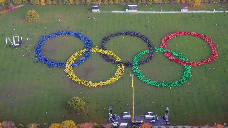 Mehrere Hundert Menschen bilden mit verschieden farbigen Ponchos im Stadtpark in Hamburg die Olympischen Ringe im Rahmen der Olympia-Initiative „Feuer und Flamme für Hamburg 2024“ nach. Links haben Olympiagegner das Wort „NO“ gebildet.