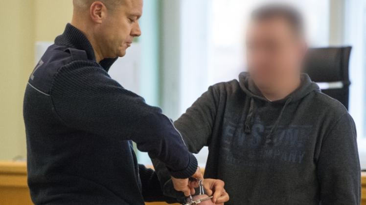 Ein Justizmitarbeiter (l.) nimmt dem Angeklagten Nick J. zum Prozessauftakt wegen versuchten Totschlag in einem Verhandlungssaal im Landgericht in Cottbus die Handschellen ab.