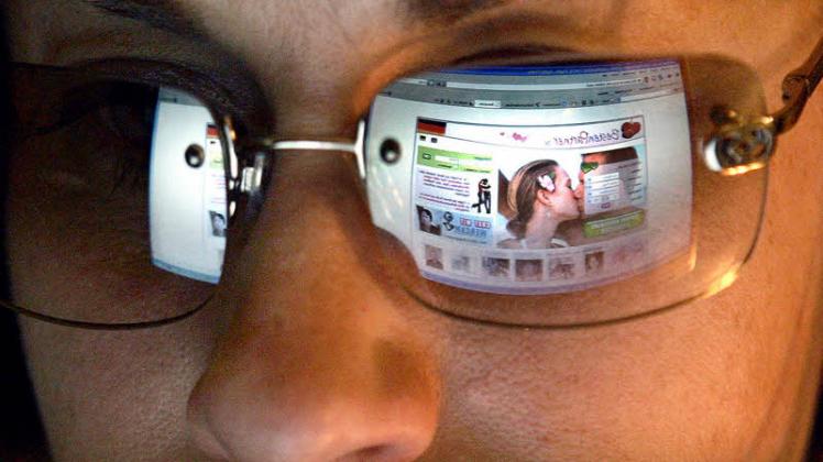Den Flirt im Blick – in der Brille einer jungen Frau spiegelt sich eine Internetseite zur Partnersuche.  