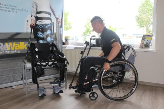 Aus dem Rollstuhl schwingt sich Dirk Janzen allein auf den Stuhl mit dem Exoskelett.