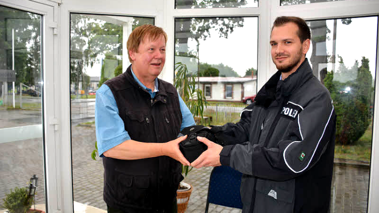 Polizeiobermeister Christian Händel gibt Pastor Gerhard Lewerenz die gestohlene Kamera zurück.  