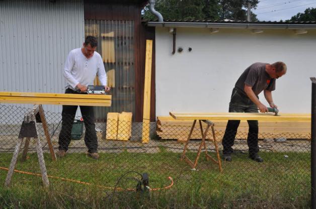 Mit Schleifgeräten bereiten Torsten Shadow (l.) und Bernd Trede die neuen Bohlen für die Bänke an der Rasenfläche vor.