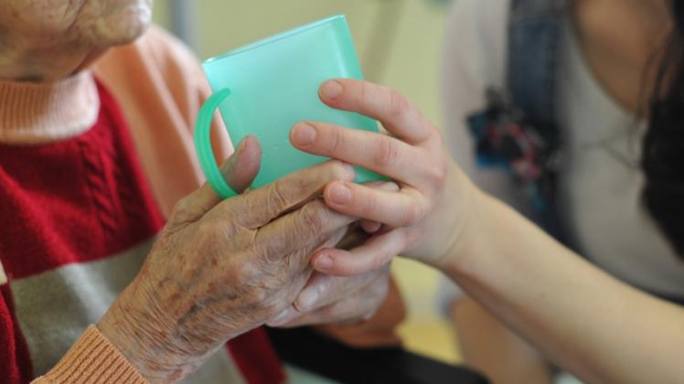 Eine Pflegerin hilft einer alten Frau beim Trinken aus einem Becher in einem Seniorenheim.  