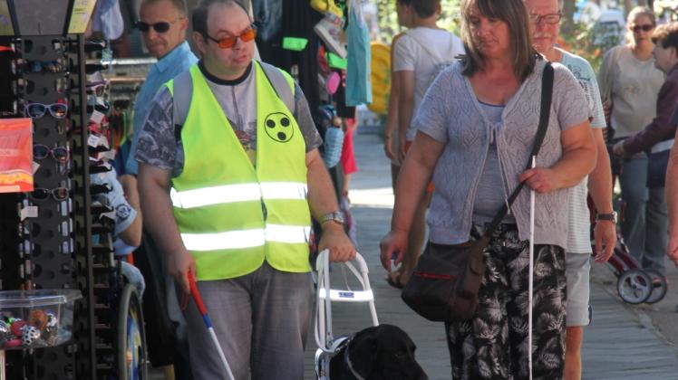 Training in der Warnemünder Mühlenstraße Marco Höster übt mit Blindenhund Coco und Trainerin Aniko Ebersberger das selbstständige Gehen mit Hund auf vollgestellten Wegen.  