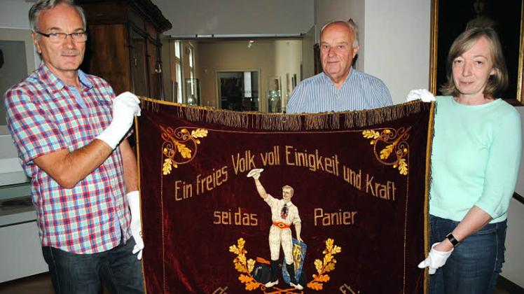Uwe Zicker, Rudi Schröder und Iris Brüdgam (v.l.) präsentieren die vermutlich ältere Vorderseite der Turnerfahne.  